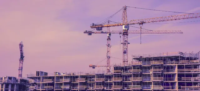 Une rangée de bâtiments en construction avec deux grues de chantier en arrière-plan.